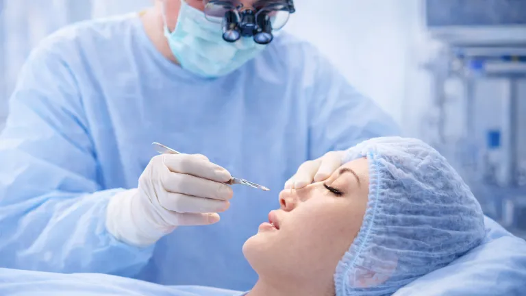 Surgeon wearing protective mask, surgical loupes and gloves performing a procedure on a patient in an operating theatre